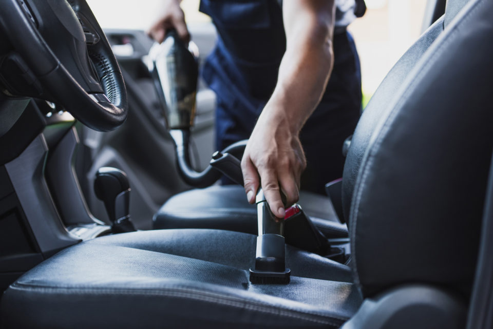 cropped view of car cleaner vacuuming drivers seat in car